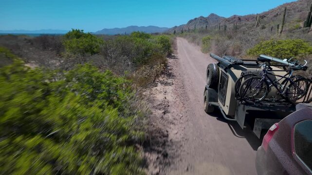 A suv pulls a teardrop camper trailer down a bumpy sand road in the Baja California desert while enjoying the overland journey