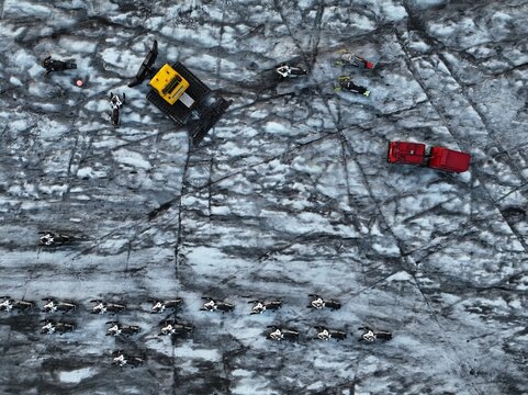 Aerial view of snowmobiles and a yellow snow groomer parked on the cracked icy surface of a glacier in Kalfafellsstadur, Sveitarfelagid Hornafjordur, Iceland.