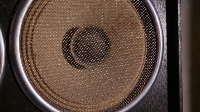 A close-up view of a vintage stereo speaker with round metal mesh grilles. Thick silver rims surround the protective wire covers. The dark textured surface highlights the retro audio design.