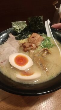 Vertical video close-up of a rich Tonkotsu ramen bowl topped with soft-boiled egg and braised pork belly