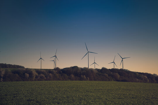 Wind turbines as silhouettes on a hill at twilight.