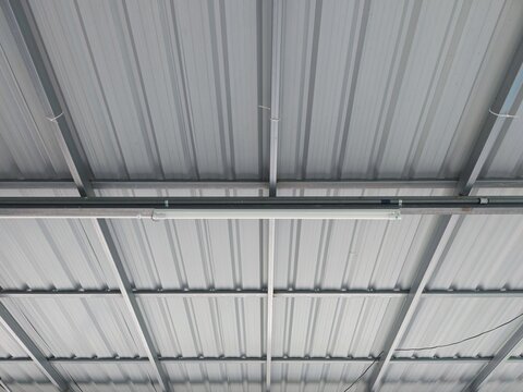 Corrugated metal sheet roof structure with steel beams in industrial building.