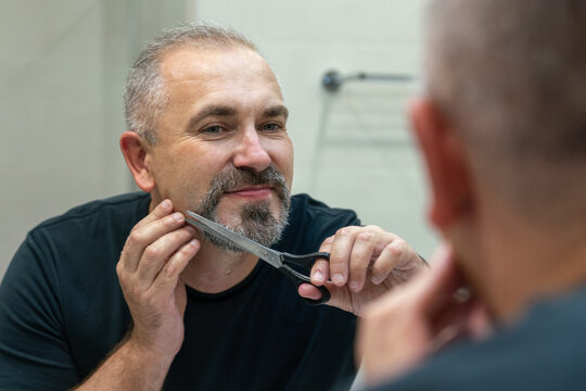 Portrait of Middle-aged handsome man cutting his beard and mooustache with scissors