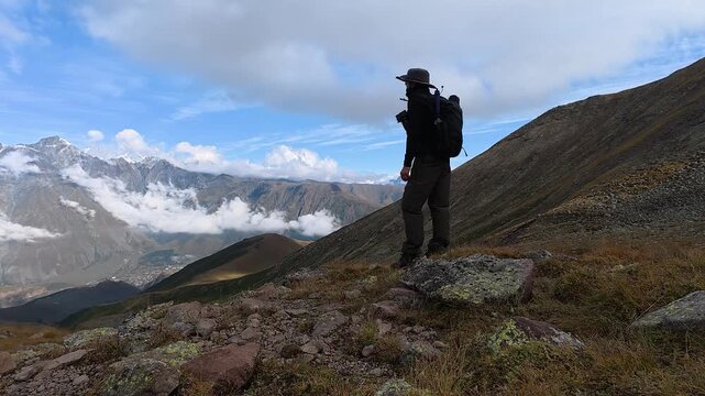 4k video of a hiker standing on a rock looking at Mount Kazbegi scenery in Georgia.