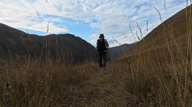 4k video of a hiker from behind walking down a grassy trail in Juta valley, Georgia.