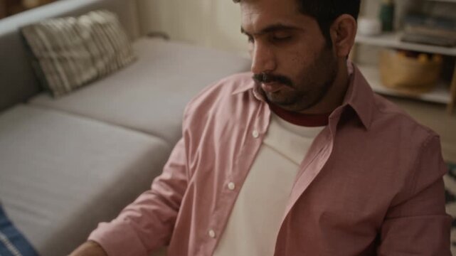 Tilt up shot of young Indian man typing on laptop, taking off glasses, and rubbing eyes to relieve fatigue. Suitable for wellness, remote work burnout, or digital eye strain campaigns