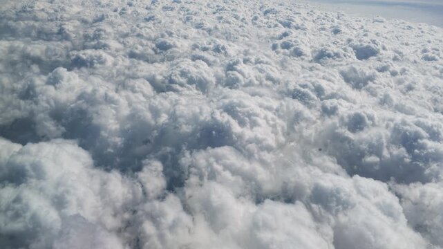 Stunning aerial view of fluffy white clouds from a flying airplane window. Beautiful cloudscape in the bright blue sky. Peaceful natural background of dramatic atmosphere high above the earth.