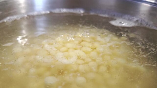 Boiling water in a stainless steel pot with small pasta shapes floating on the surface, bubbles forming as the heat intensifies in a kitchen setting