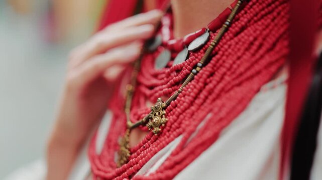 Detailed macro shot focusing on a multi-strand red coral necklace with antique metal accents worn over a white vyshyvanka. Highlighting the timeless beauty of authentic Ukrainian folk ornamentation.
