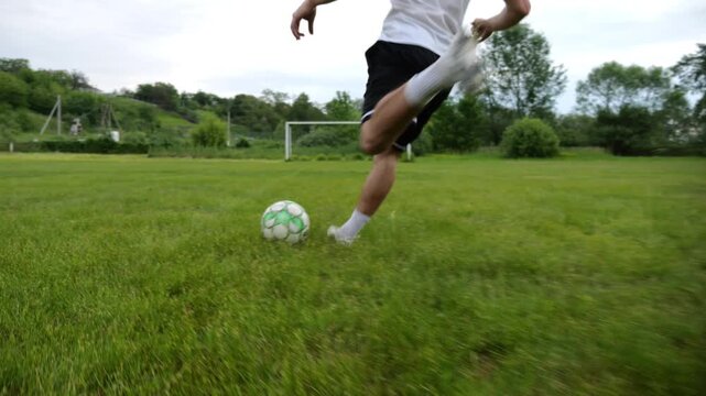 Leg of sportsman shooting a penalty kicks on stadium at summer day. Male foot of professional footballer kicking ball at green field. Young man training at meadow. Concept of a freestyle football