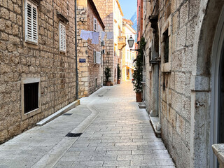 Obraz premium Narrow cobblestone alley between historic limestone buildings with laundry hanging overhead in Makarska old town, Croatia