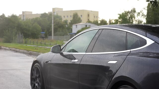 Modern electrical automobile driving at urban road on rainy day. Ecology friendly car riding moving along motorway. Electric vehicle riding through empty highway. Concept of green innovation. Slow mo