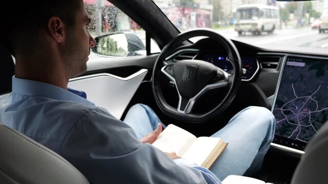 Male businessperson reading book during riding on electrical vehicle with autopilot at rainy day. Successful businessman improving knowledge while ride an autonomous self driving electric car at city