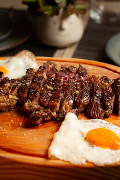 Sliced medium-rare beef steak with two fried eggs served on a wooden board.