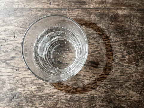 Vaso de vidrio con marca circular de agua sobre mesa de madera, plano cenital