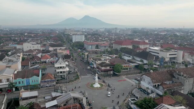 Drone footage of Tugu Yogyakarta, an iconic historic landmark located in the heart of Yogyakarta, Indonesia. Aerial view captures the striking white monument standing prominently at a busy city inters