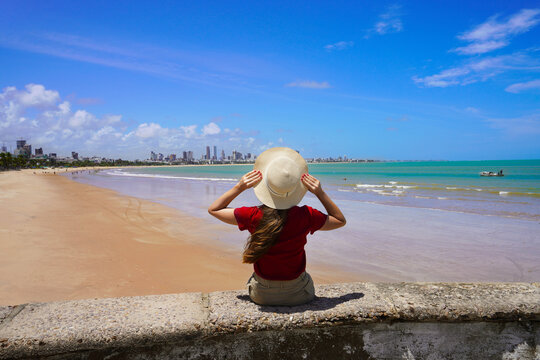 Vacation in Joao Pessoa, Brazil. Back view of young woman sitting on wall enjoying Joao Pessoa beach on northeast coast of Brazil.