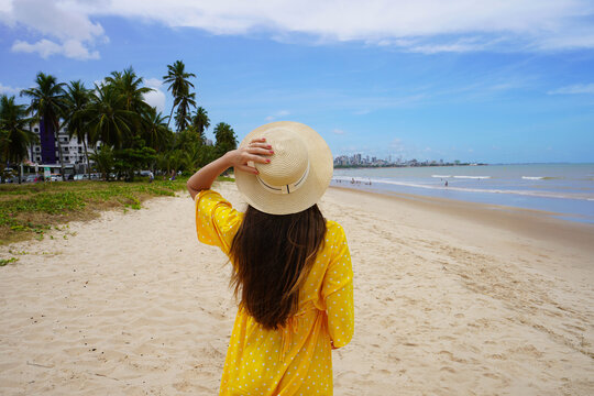 Holidays in Joao Pessoa, Brazil. Back view of young woman with yellow sundress on Praia de Cabo Branco beach, Joao Pessoa, Brazil.