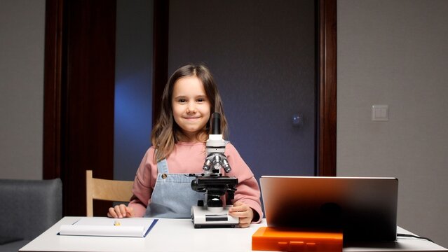 Curious young student exploring the micro world with a microscope and laptop at home, engaging in a science experiment and hands on education
