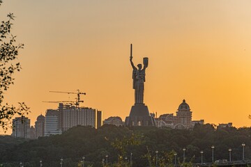 Kyiv Motherland Monument and Rio de Janeiro cityscape, dominated by Christ the Redeemer statue against a sunset backdrop Diverse architecture with modern high-rises and older structures Golden hour © Mister