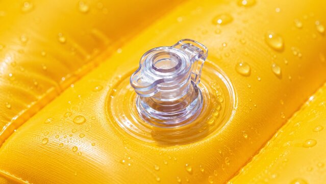 Detailed macro photography of a transparent plastic air valve stopper on a shiny yellow PVC pool float
