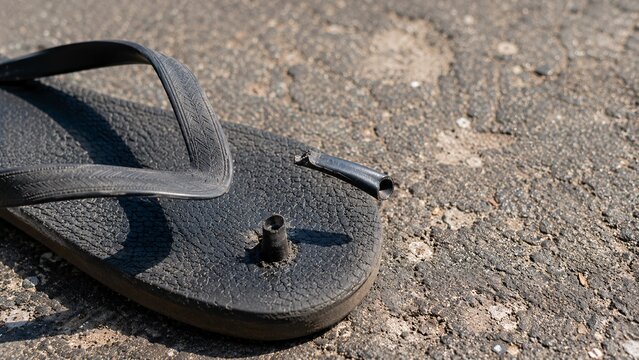 Close-up of a broken black rubber flip flop sandal with a blown-out strap abandoned on rough street asphalt
