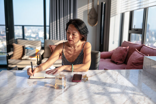 Woman writing in notebook with city view in background.