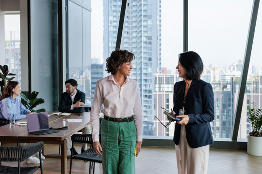 Businesswomen converse in a modern office with city view