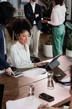 Business meeting with diverse team, woman working on digital tablet.