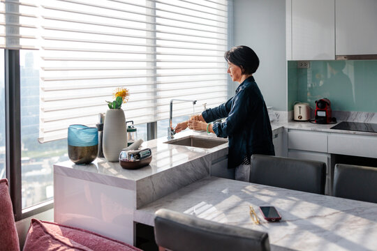 Woman filling glass with water at kitchen sink