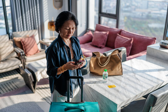 Woman with luggage checks phone in modern hotel room.