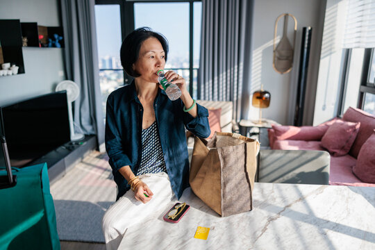 Woman drinks water in bright, modern apartment.