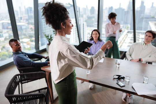 Businesswoman presents to colleagues in modern office with city view.