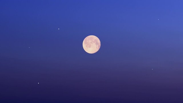 Full Moon on a twilight sky with landscape and tree silhouettes.