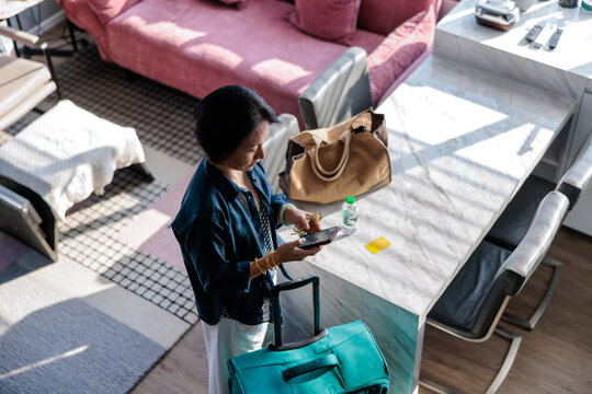 Woman with luggage checks phone in modern apartment.