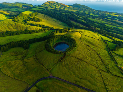 Aerial view of the volcanic crater lake surrounded by lush green hills and dense forests near the Miradouro do Pico do Carvao in Arrifes, Acores, Portugal.