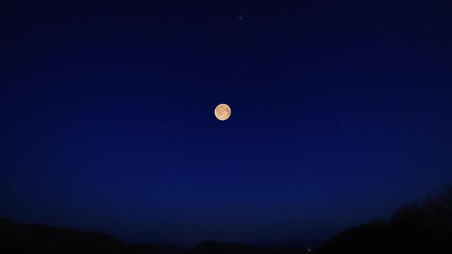 Full Moon on a twilight sky with landscape and tree silhouettes.
