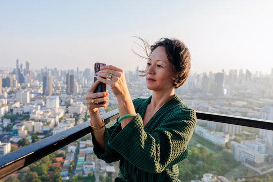 Woman in robe photographs city skyline from high rise balcony