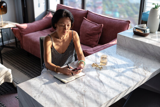 Woman with phone and notebook at marble table.