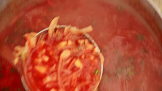 Stirring borscht in pot, vibrant red soup with herbs and vegetables visible
