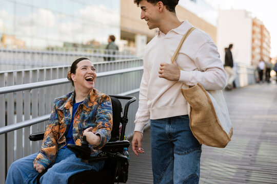 Woman in wheelchair laughing with man in urban setting