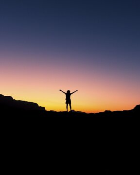 Happy celebrating winning success woman at sunset or sunrise standing elated with arms raised up in celebration of having reached mountain top summit goal during hiking travel trek