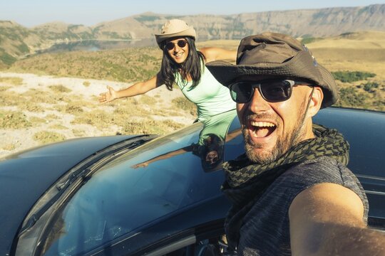 Happy young caucasian couple taking selfie while sitting in rented vehicle black car having road trip Europe. Outdoor lifestyle activity on road trip vacation concept. Excited happy couple enjoy ride