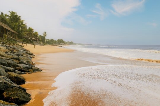 Sri Lanka sandy beach shoreline with gentle waves palm trees coastal huts rocks warm light serene tropical seascape travel scenery