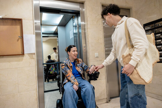 Young man assisting woman in electric wheelchair entering elevator