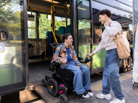 Young woman in wheelchair boarding bus with assistance