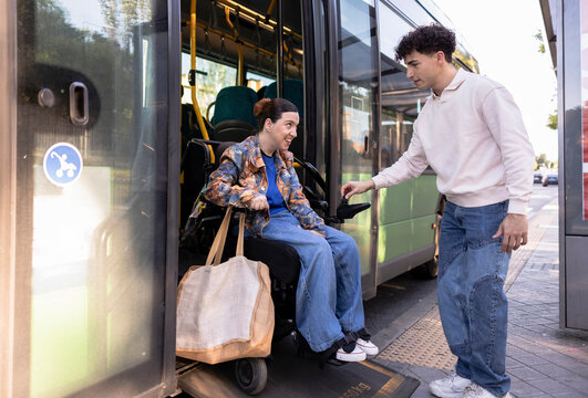 Man assisting woman in power wheelchair boarding public bus