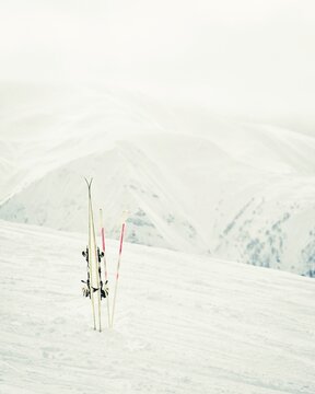 Pair of white skis with poles planted in snow on mountain slope with alpine peaks in background, concept of winter sport, ski holiday, rentals, quality gear and day off from slopes