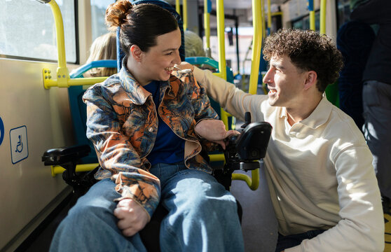 Young woman in wheelchair chatting with friend on bus