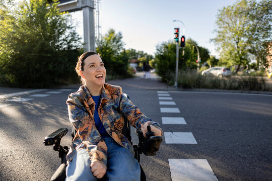 Happy woman operating electric wheelchair at crosswalk